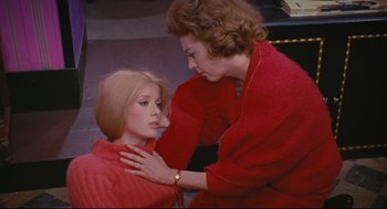 Movie still from “The Umbrellas of Cherbourg” (1964), directed by Jacques Demy – A woman in a red sweater is touching the neck of another woman; Medium shot, High angle