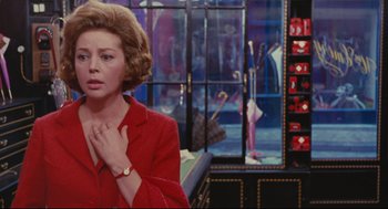 Movie still from “The Umbrellas of Cherbourg” (1964), directed by Jacques Demy – A woman in a red jacket standing in front of a window; Medium shot, Over the shoulder angle