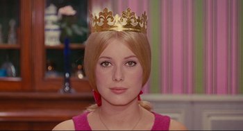 Movie still from “The Umbrellas of Cherbourg” (1964), directed by Jacques Demy – A woman wearing a gold crown and a pink dress; Close Up shot, Low angle