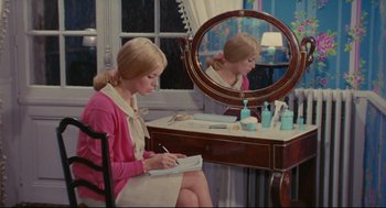 Movie still from “The Umbrellas of Cherbourg” (1964), directed by Jacques Demy – A woman sitting in front of a mirror writing in a notebook; Medium shot, High angle