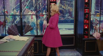 Movie still from “The Umbrellas of Cherbourg” (1964), directed by Jacques Demy – A woman in a pink coat is walking by a window; Wide shot, Over the shoulder angle