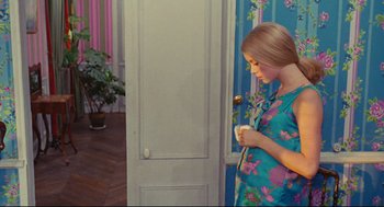 Movie still from “The Umbrellas of Cherbourg” (1964), directed by Jacques Demy – A young girl standing in front of a door; Medium shot, Over the shoulder angle