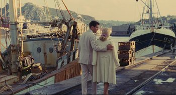 Movie still from “The Umbrellas of Cherbourg” (1964), directed by Jacques Demy – A man and a woman standing next to each other on a dock; Wide shot, High angle