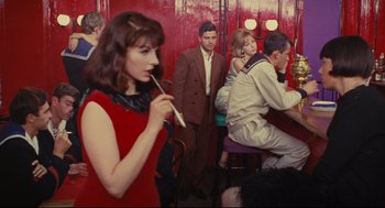 Movie still from “The Umbrellas of Cherbourg” (1964), directed by Jacques Demy – A group of people sitting at a table in front of a woman; Medium shot, High angle