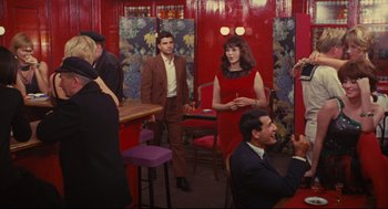 Movie still from “The Umbrellas of Cherbourg” (1964), directed by Jacques Demy – A group of people standing around in a room; Wide shot, High angle