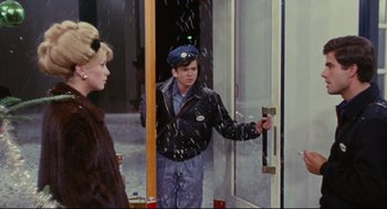 Movie still from “The Umbrellas of Cherbourg” (1964), directed by Jacques Demy – A man in a blue hat is opening the door to a building; Medium shot, Over the shoulder angle