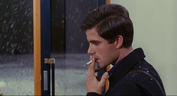 Movie still from “The Umbrellas of Cherbourg” (1964), directed by Jacques Demy – A man smoking a cigarette while wearing a jacket; Close Up shot, Over the shoulder angle