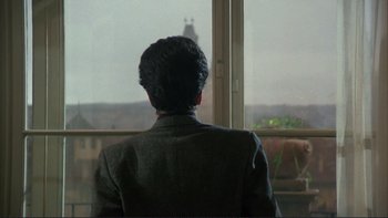 Movie still from “The Unbearable Lightness of Being” (1988), directed by Philip Kaufman – A man in a suit looking out of a window; Medium shot, Over the shoulder angle