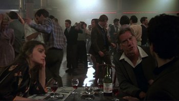 Movie still from “The Unbearable Lightness of Being” (1988), directed by Philip Kaufman – A group of people sitting at a table with wine glasses; Medium shot, Over the shoulder angle