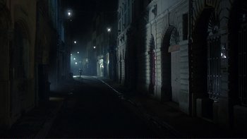 Movie still from “The Unbearable Lightness of Being” (1988), directed by Philip Kaufman – A dark street with a person walking down the sidewalk; Extreme Wide shot, High angle