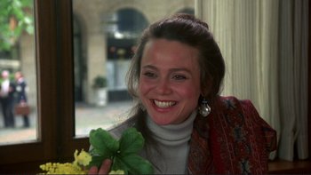 Movie still from “The Unbearable Lightness of Being” (1988), directed by Philip Kaufman – A woman smiling while holding a flower in her hand; Close Up shot, Over the shoulder angle