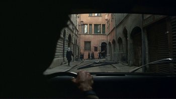 Movie still from “The Unbearable Lightness of Being” (1988), directed by Philip Kaufman – A view from inside a car looking out the window at people walking down the street; Wide shot, High angle