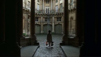 Movie still from “The Unbearable Lightness of Being” (1988), directed by Philip Kaufman – A woman is walking through a courtyard with luggage; Extreme Wide shot, High angle
