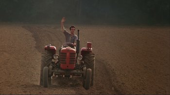 Movie still from “The Unbearable Lightness of Being” (1988), directed by Philip Kaufman – A man driving a tractor on a dirt field; Wide shot, High angle
