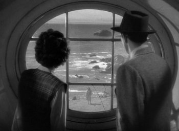 Movie still from “The Uninvited” (1944), directed by Lewis Allen – A man and a woman looking out of a window at the beach; Extreme Wide shot, High angle