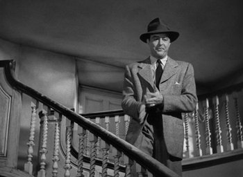 Movie still from “The Uninvited” (1944), directed by Lewis Allen – A man in a suit and hat standing on a staircase; Medium shot, Low angle