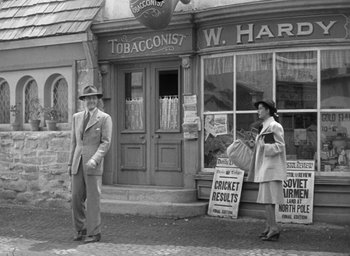 Movie still from “The Uninvited” (1944), directed by Lewis Allen – A man and a woman standing in front of tobacconist shop; Wide shot, Low angle