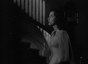 Movie still from “The Uninvited” (1944), directed by Lewis Allen – A woman in a white dress standing in front of a staircase; Medium shot, Low angle