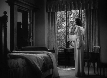 Movie still from “The Uninvited” (1944), directed by Lewis Allen – A black and white photo of a woman standing in front of a window; Wide shot, Over the shoulder angle