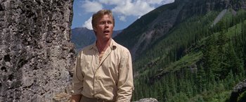 Movie still from “The Unsinkable Molly Brown” (1964), directed by Charles Walters – A man standing on top of a mountain near a forest; Medium shot, Low angle