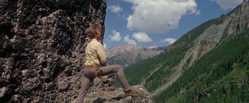 Movie still from “The Unsinkable Molly Brown” (1964), directed by Charles Walters – A man sitting on top of a rock on top of a mountain; Wide shot, Low angle