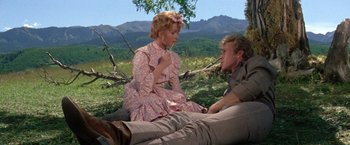 Movie still from “The Unsinkable Molly Brown” (1964), directed by Charles Walters – A man and a woman sitting on the ground in a field; Medium shot, High angle