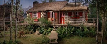Movie still from “The Unsinkable Molly Brown” (1964), directed by Charles Walters – An old log cabin with a porch and a wooden bench; Extreme Wide shot, High angle