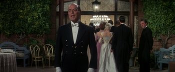 Movie still from “The Unsinkable Molly Brown” (1964), directed by Charles Walters – A man in a tuxedo standing in front of a group of people; Medium shot, Over the shoulder angle