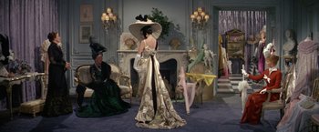 Movie still from “The Unsinkable Molly Brown” (1964), directed by Charles Walters – A woman in a long dress and a large hat in front of a fireplace; Wide shot, Over the shoulder angle
