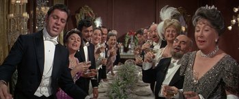 Movie still from “The Unsinkable Molly Brown” (1964), directed by Charles Walters – A group of people sitting at a dinner table drinking wine; Medium shot, High angle