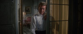 Movie still from “The Unsinkable Molly Brown” (1964), directed by Charles Walters – A man in a white shirt and black pants standing in front of a window; Medium shot, Over the shoulder angle