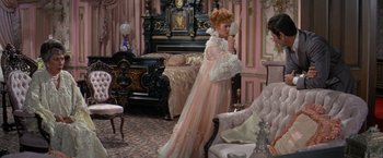 Movie still from “The Unsinkable Molly Brown” (1964), directed by Charles Walters – A woman in a pink dress holding a mirror in a living room; Wide shot, High angle
