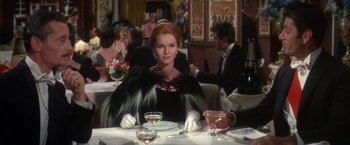 Movie still from “The Unsinkable Molly Brown” (1964), directed by Charles Walters – A woman sitting at a table with a glass of wine in front of her; Medium shot, Over the shoulder angle