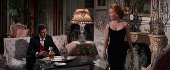 Movie still from “The Unsinkable Molly Brown” (1964), directed by Charles Walters – A woman in a black dress standing in front of a table; Medium shot, Over the shoulder angle