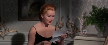 Movie still from “The Unsinkable Molly Brown” (1964), directed by Charles Walters – A woman in a black top is reading a paper; Close Up shot, Over the shoulder angle