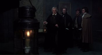 Movie still from “The Vampire Lovers” (1970), directed by Roy Ward Baker – A group of men standing next to each other in front of a lantern; Medium shot, Over the shoulder angle