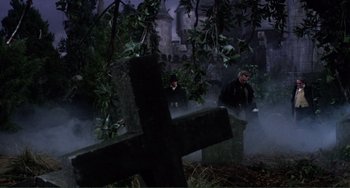 Movie still from “The Vampire Lovers” (1970), directed by Roy Ward Baker – Two men standing next to each other near a cross; Wide shot, Low angle