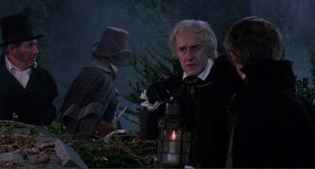 Movie still from “The Vampire Lovers” (1970), directed by Roy Ward Baker – A man in a black coat and a white beard holding a lantern; Medium shot, Over the shoulder angle
