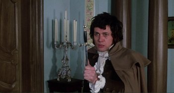 Movie still from “The Vampire Lovers” (1970), directed by Roy Ward Baker – A man holding a sword in a room with candles; Medium shot, Over the shoulder angle