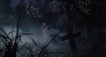 Movie still from “The Vampire Lovers” (1970), directed by Roy Ward Baker – A woman in a white dress standing in front of a cross; Wide shot, High angle