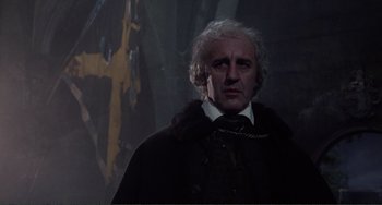 Movie still from “The Vampire Lovers” (1970), directed by Roy Ward Baker – A man in a black coat and a chain around his neck; Medium shot, Low angle