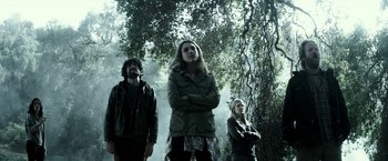 Movie still from “The Veil” (2016), directed by Phil Joanou – A group of people standing next to each other in the woods; Medium shot, Low angle