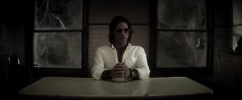 Movie still from “The Veil” (2016), directed by Phil Joanou – A man sitting at a table in front of a brick wall; Medium shot, Low angle