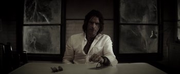 Movie still from “The Veil” (2016), directed by Phil Joanou – A man sitting at a table holding a pair of eyeglasses; Close Up shot, Low angle