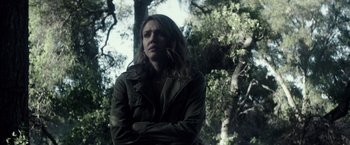 Movie still from “The Veil” (2016), directed by Phil Joanou – A woman standing in front of a tree with her arms crossed; Medium shot, Over the shoulder angle