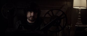 Movie still from “The Veil” (2016), directed by Phil Joanou – A man holding a movie projector in a dark room; Close Up shot, High angle