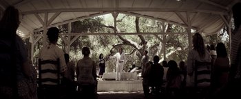 Movie still from “The Veil” (2016), directed by Phil Joanou – A man standing on top of a stage in front of a crowd of onlookers; Wide shot, Over the shoulder angle