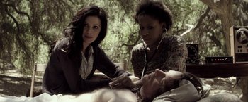 Movie still from “The Veil” (2016), directed by Phil Joanou – A man laying on the ground next to two women; Medium shot, High angle