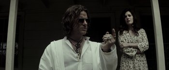 Movie still from “The Veil” (2016), directed by Phil Joanou – A man with long hair wearing a white shirt and sunglasses; Close Up shot, Low angle