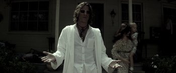 Movie still from “The Veil” (2016), directed by Phil Joanou – A man in a white shirt and tie standing in front of a house; Medium shot, Low angle